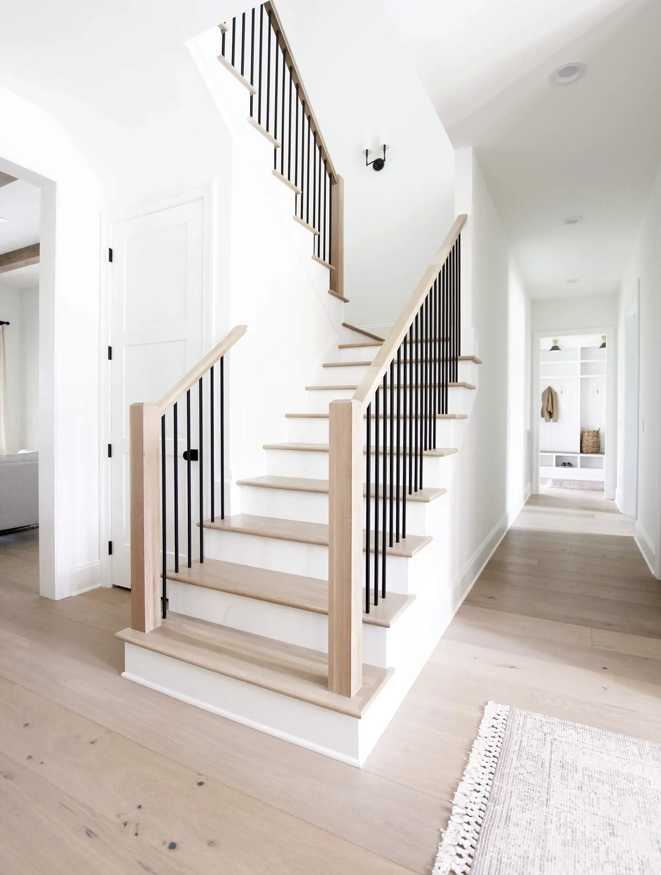 Newly built staircase with white oak treads and matte black square balusters, leading to a bright hallway